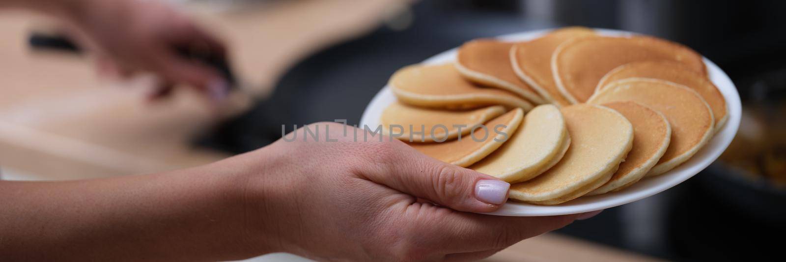 Woman holding plate of pancakes near stove in kitchen closeup. Rustic cuisine concept