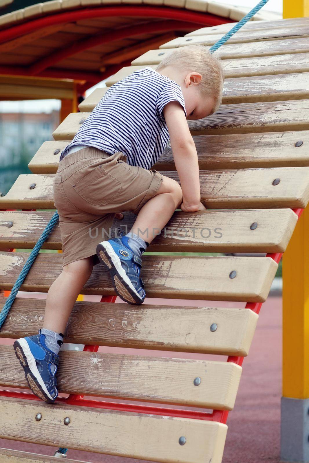 Kid on a wooden climbing wal stubbornly climbs up by Lincikas