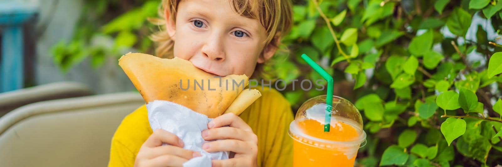 Sweet little caucasian boy, eating pancakes and drinking orange juice. BANNER, LONG FORMAT