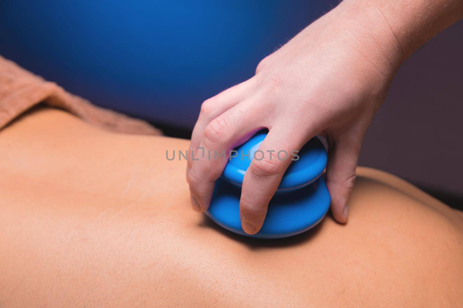 Close-up of a man's back with rubber vacuum cans installed in a dark room of a spa salon.