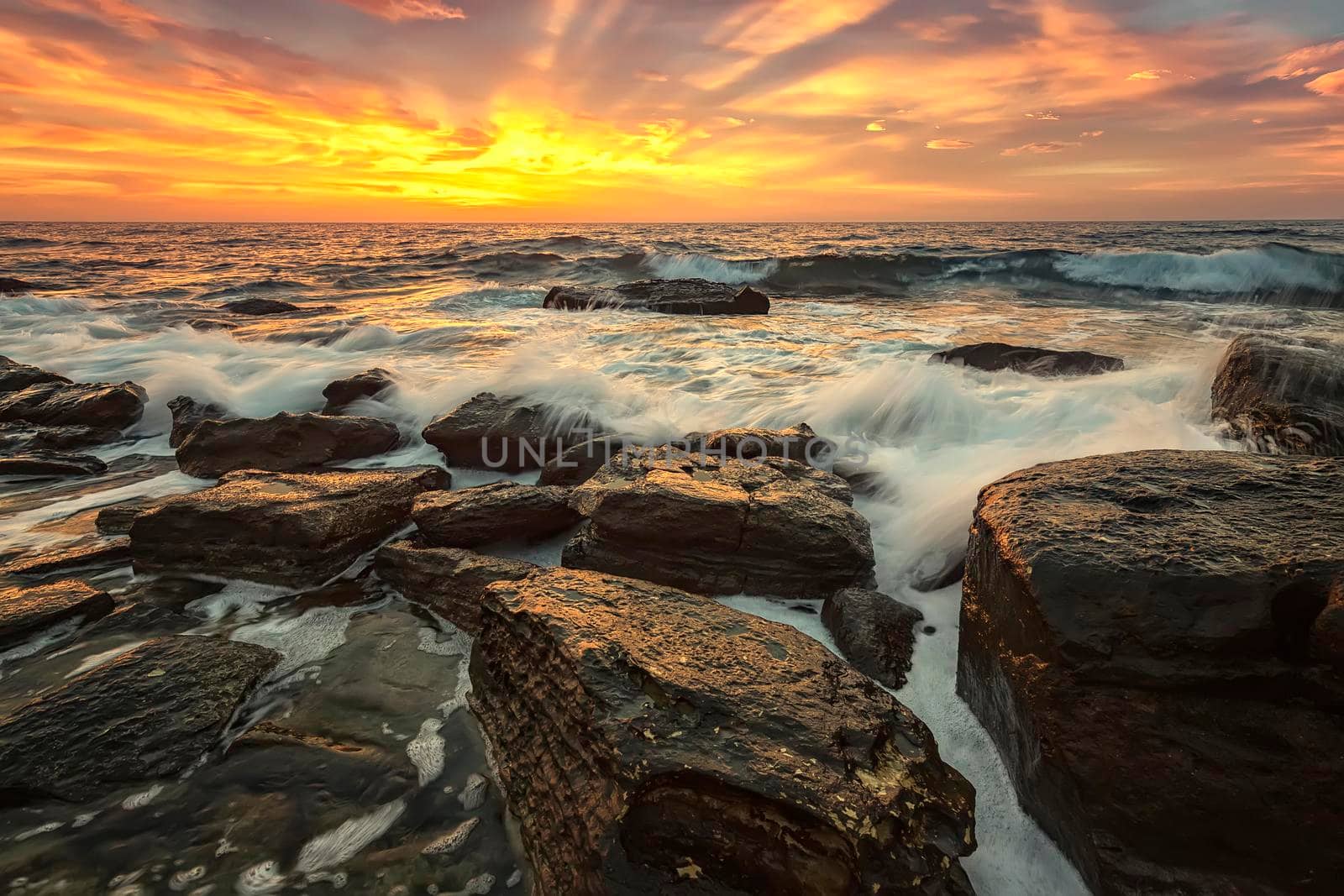 The stunning seascape with the colorful sky and first rays at the rocky coastline of the Black Sea