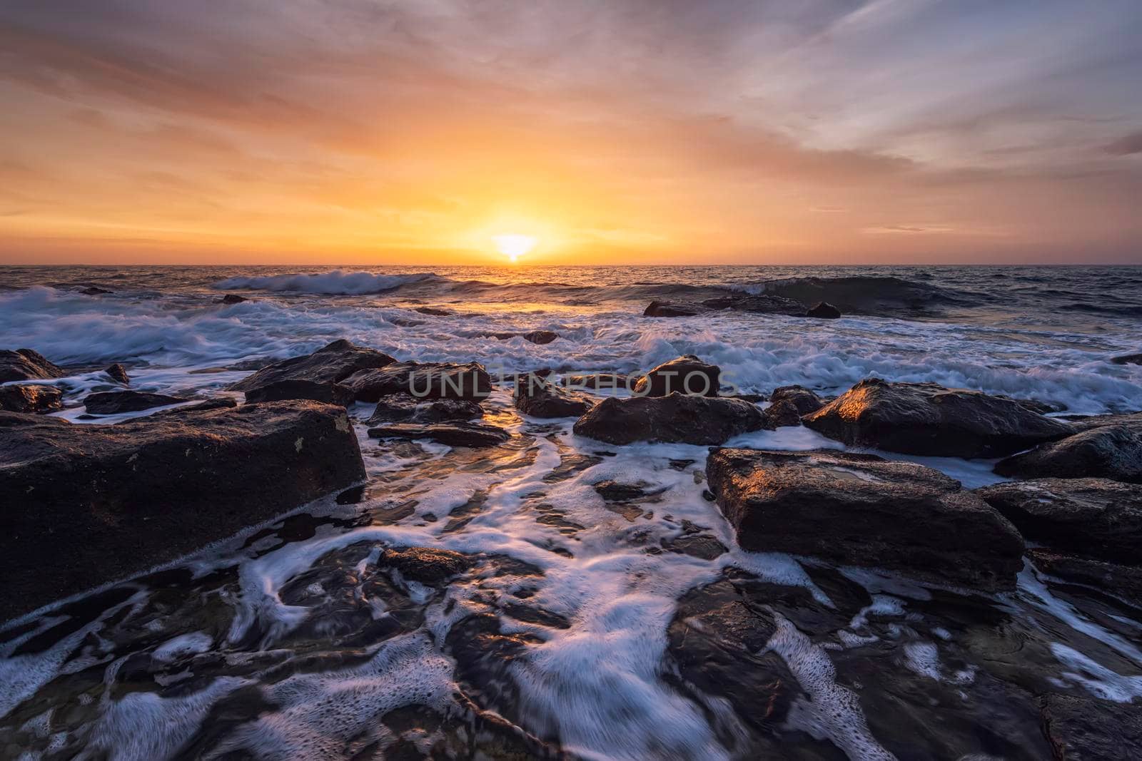 The stunning seascape with the colorful sky and water foam at the rocky coastline of the Black Sea