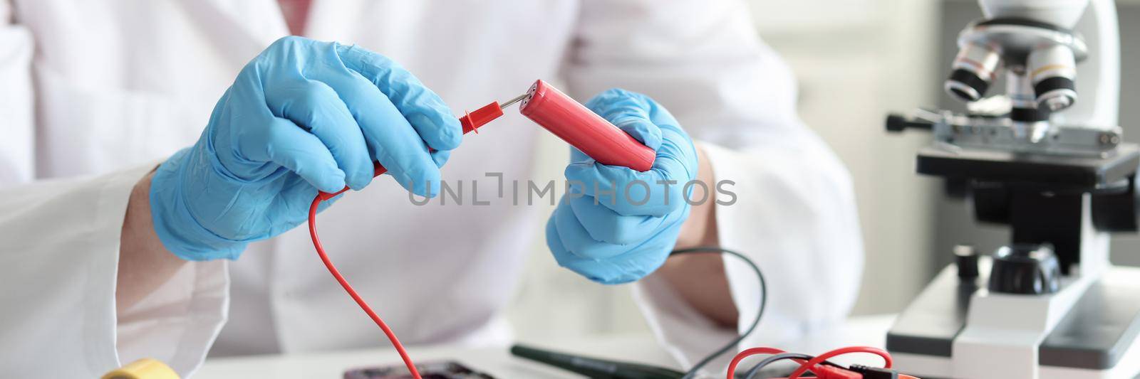 Master repairman checking battery charge using tester closeup. Electronics diagnostics concept