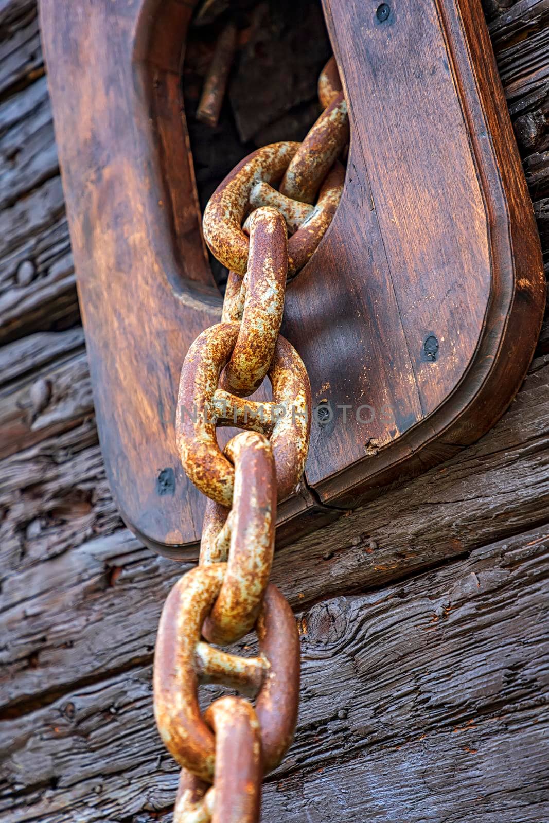 View of rusty anchor chain coming out of a wooden sailing ship. Vertical view