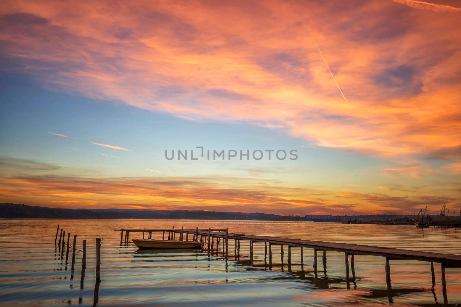 Magnificent sunset at the seashore with wooden pier and boat.