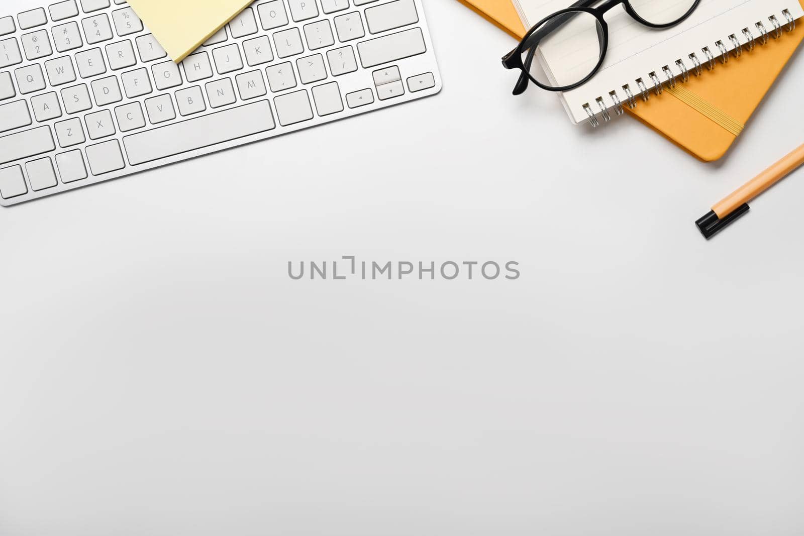 Flat lay wireless keyboard, notebook, eyeglasses and pen on white table. Copy space for your text.