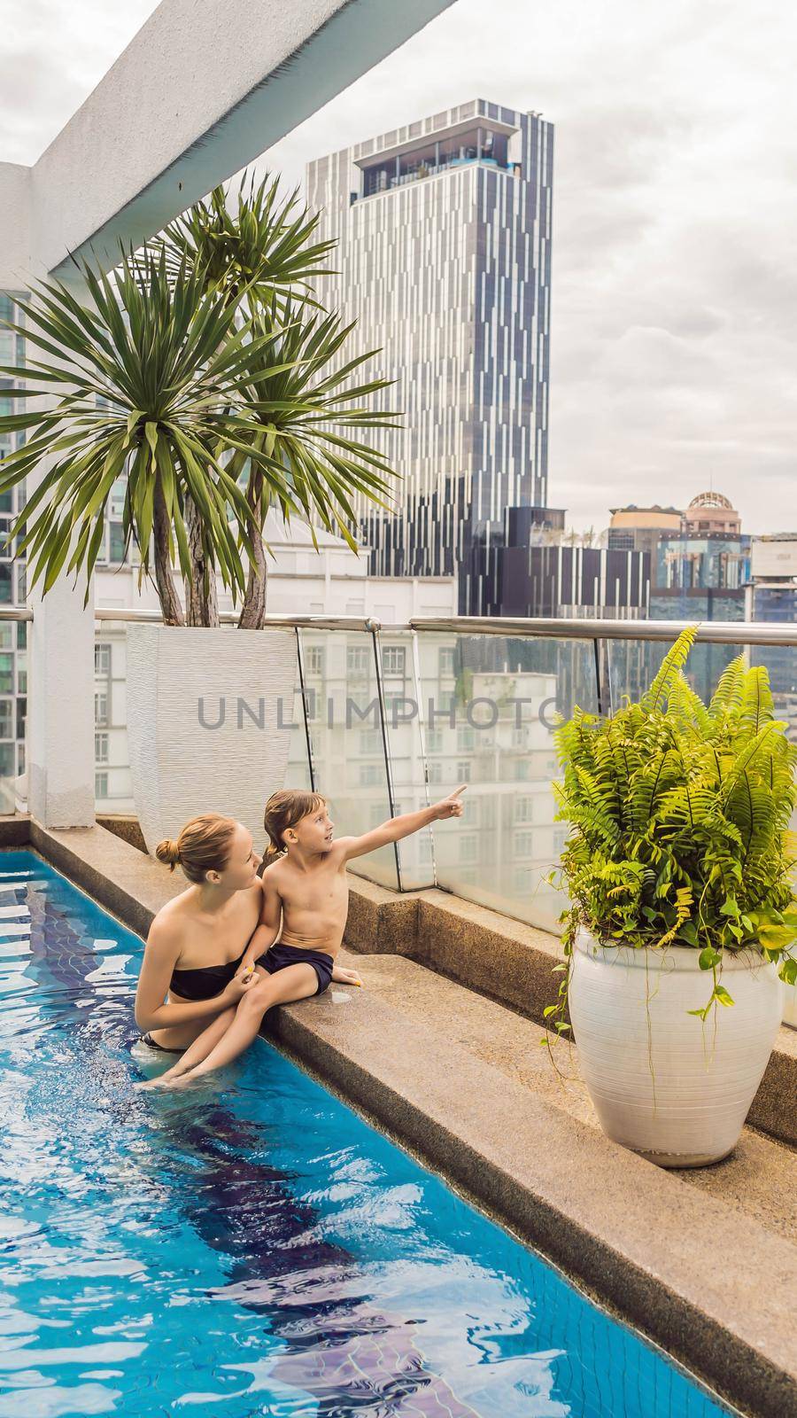 Malaysia, Kuala Lumpur November 21, 2018: Mother and son in the pool among the skyscrapers and the big city. Relax in the big city. Rest from stress. VERTICAL FORMAT for Instagram mobile story or stories size. Mobile wallpaper