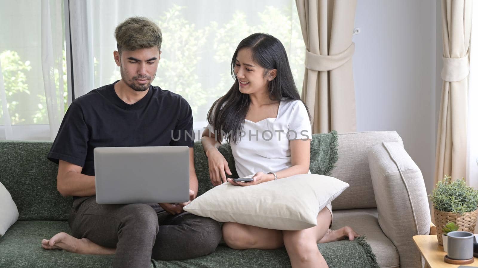 Loving asian couple relaxing on comfortable couch and surfing internet with computer laptop together.