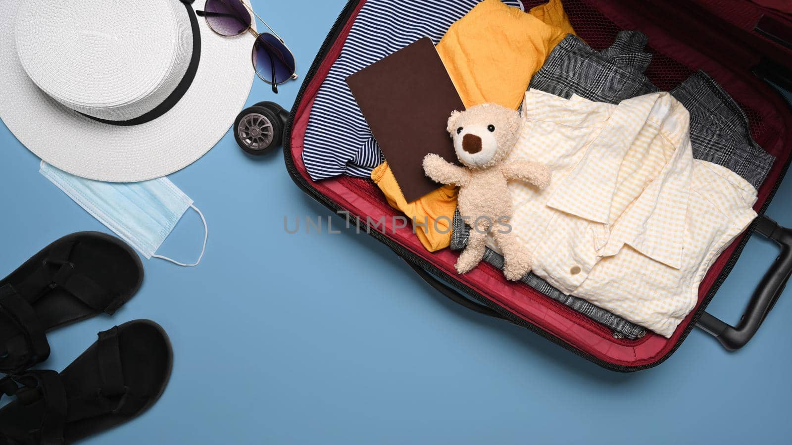 Top view open suitcase with casual clothes and passports over blue background. Holidays, travel, tourism, flight luggage concept.