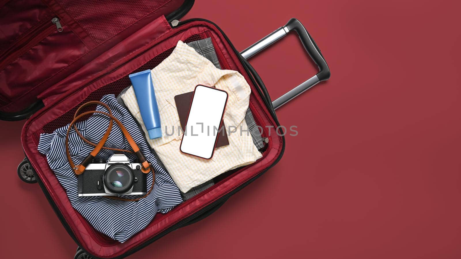Open travel bag with clothes, film camera smart phone and passports on red background. Packing for a new journey.