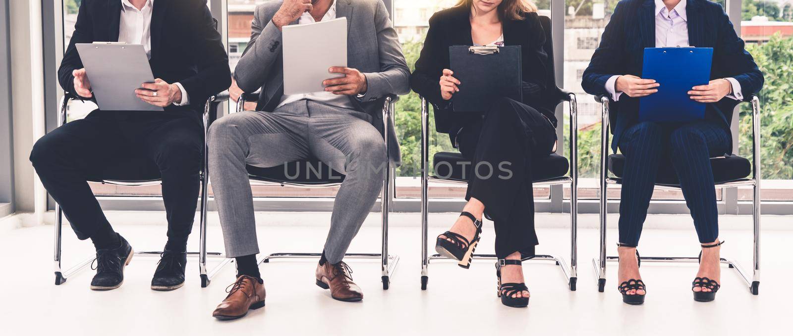 Businesswomen and businessmen holding resume CV folder while waiting on chairs in office for job interview. Corporate business and human resources concept.