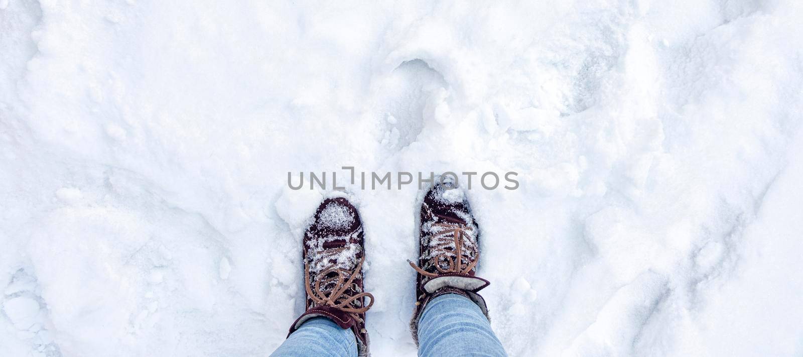 banner with Legs in burgundy boots and blue jeans in the snow. Footprints in the snow. Winter landscape. Soft focus. Top view
