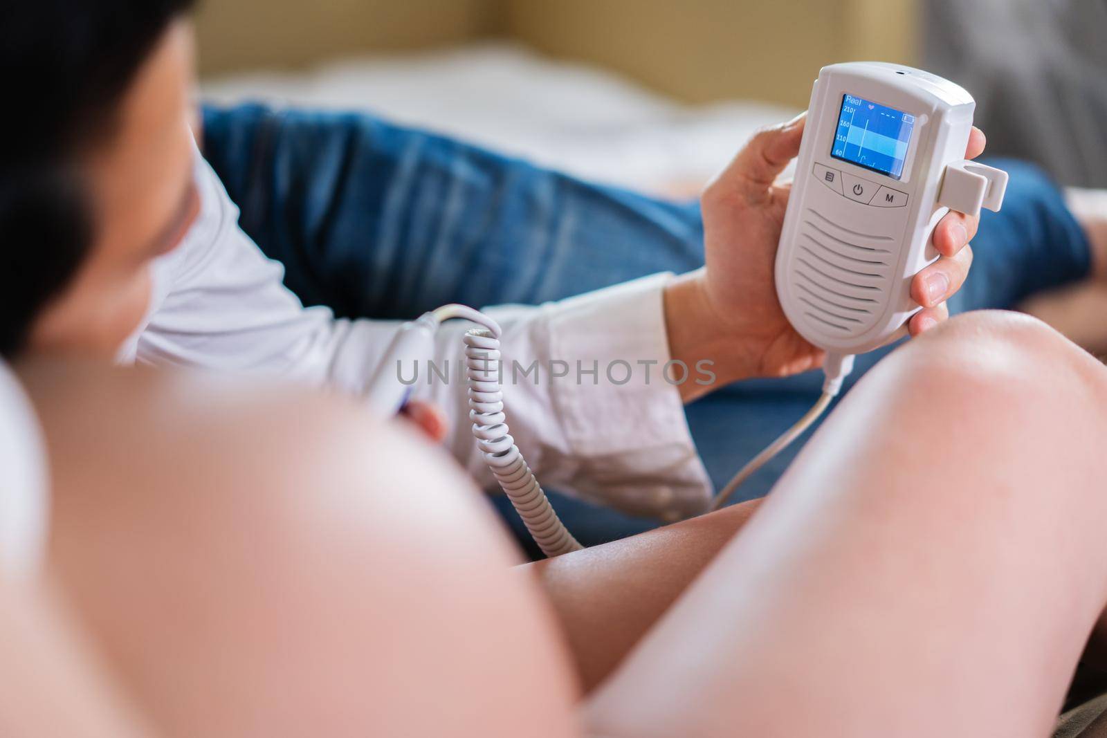 pregnant woman and her husband using fetal droppler device for listening baby heartbeat by geargodz