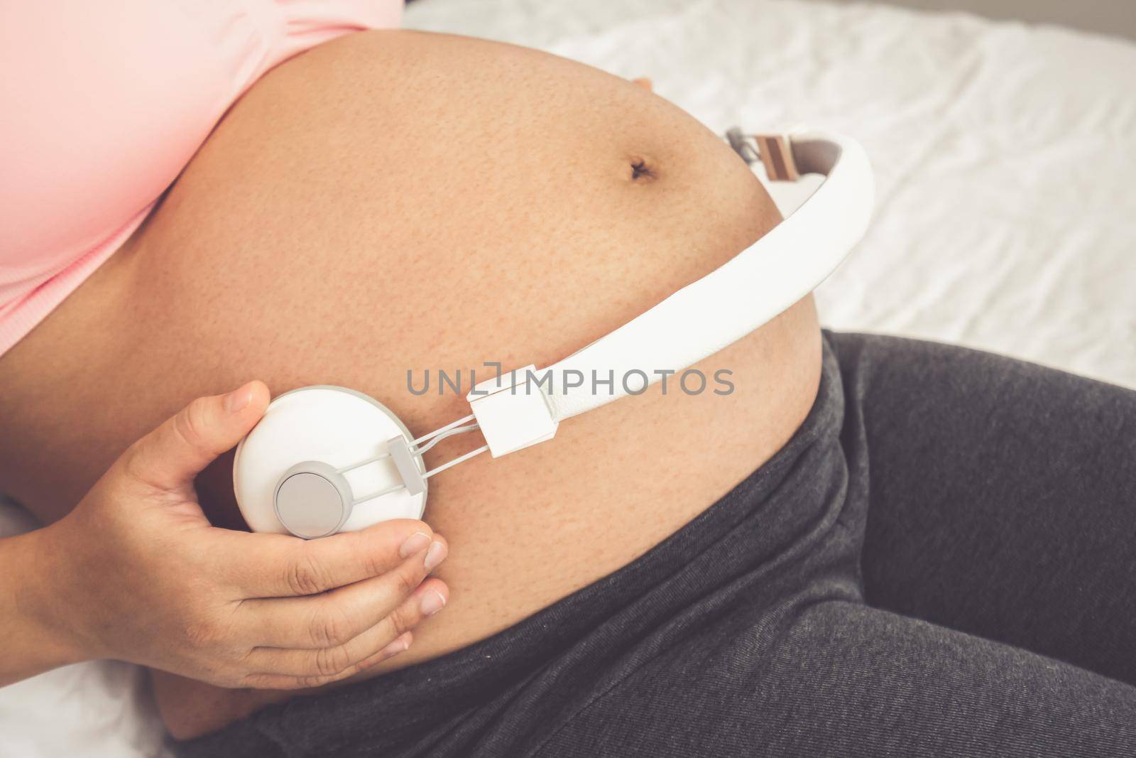 Pregnant woman feeling happy at home while taking care of her child. The young expecting mother holding baby in pregnant belly. Maternity prenatal care and woman pregnancy concept.