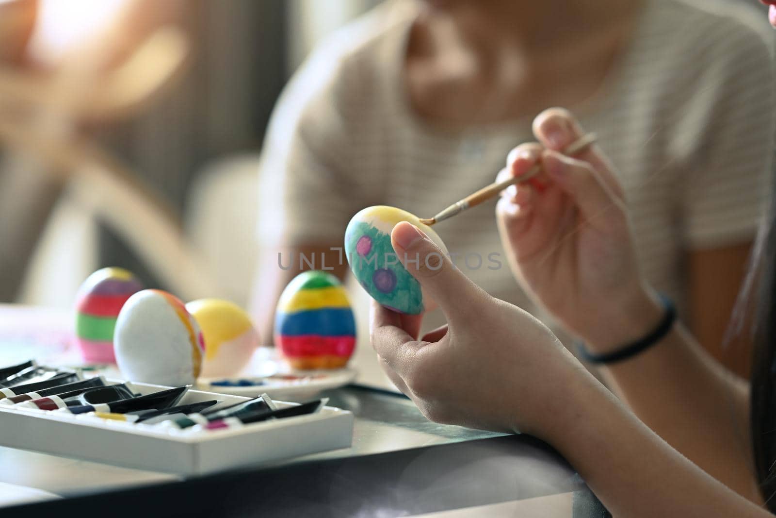 Close up view little girl holding paintbrush painting on egg for Easter festival. Easter, holidays and people concept. by prathanchorruangsak