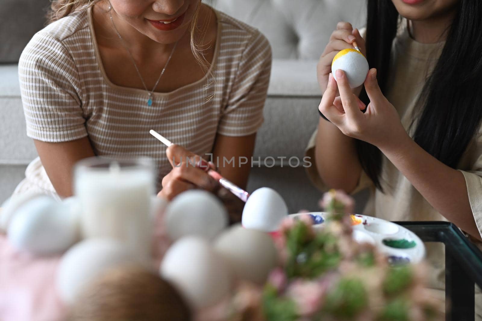 Mother and daughter spending time together before Easter festival and painting colorful Easter eggs.
