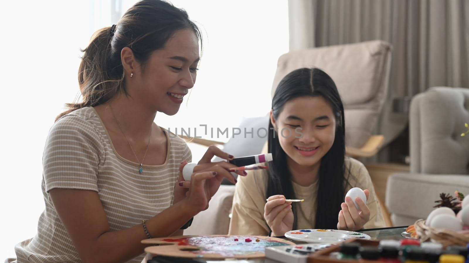 Happy family painting Easter eggs together while sitting in bright living room. Easter holidays and people concept. by prathanchorruangsak