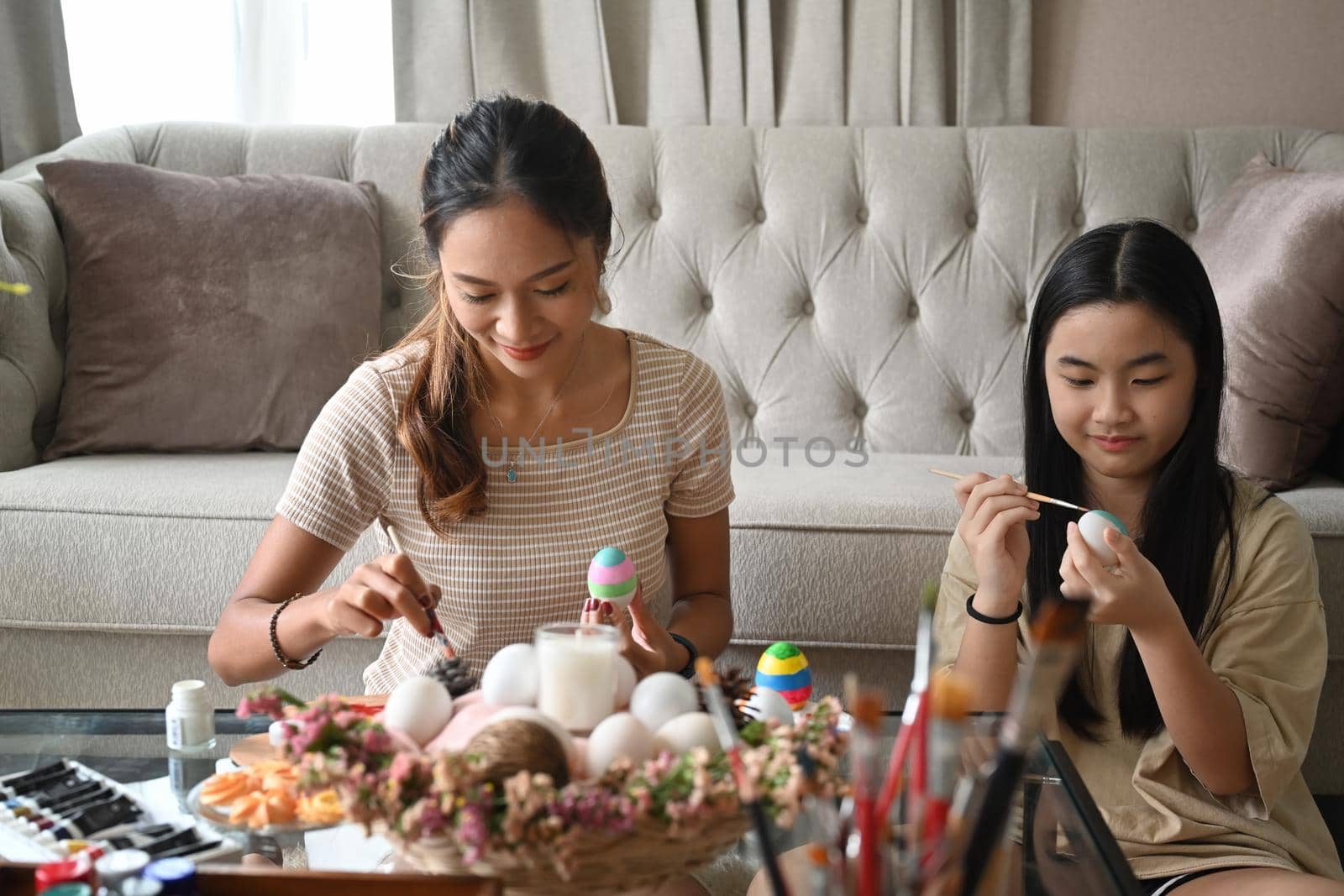 A mother and her daughter painting Easter eggs, preparing for Easter festival. by prathanchorruangsak