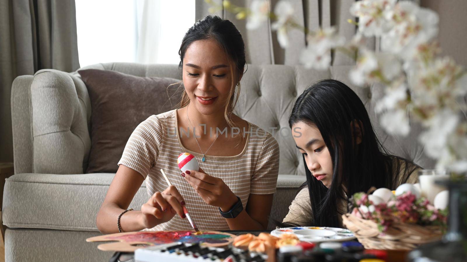 Happy mother and daughter enjoy painting eggs while preparing for Easter egg festival at home. by prathanchorruangsak