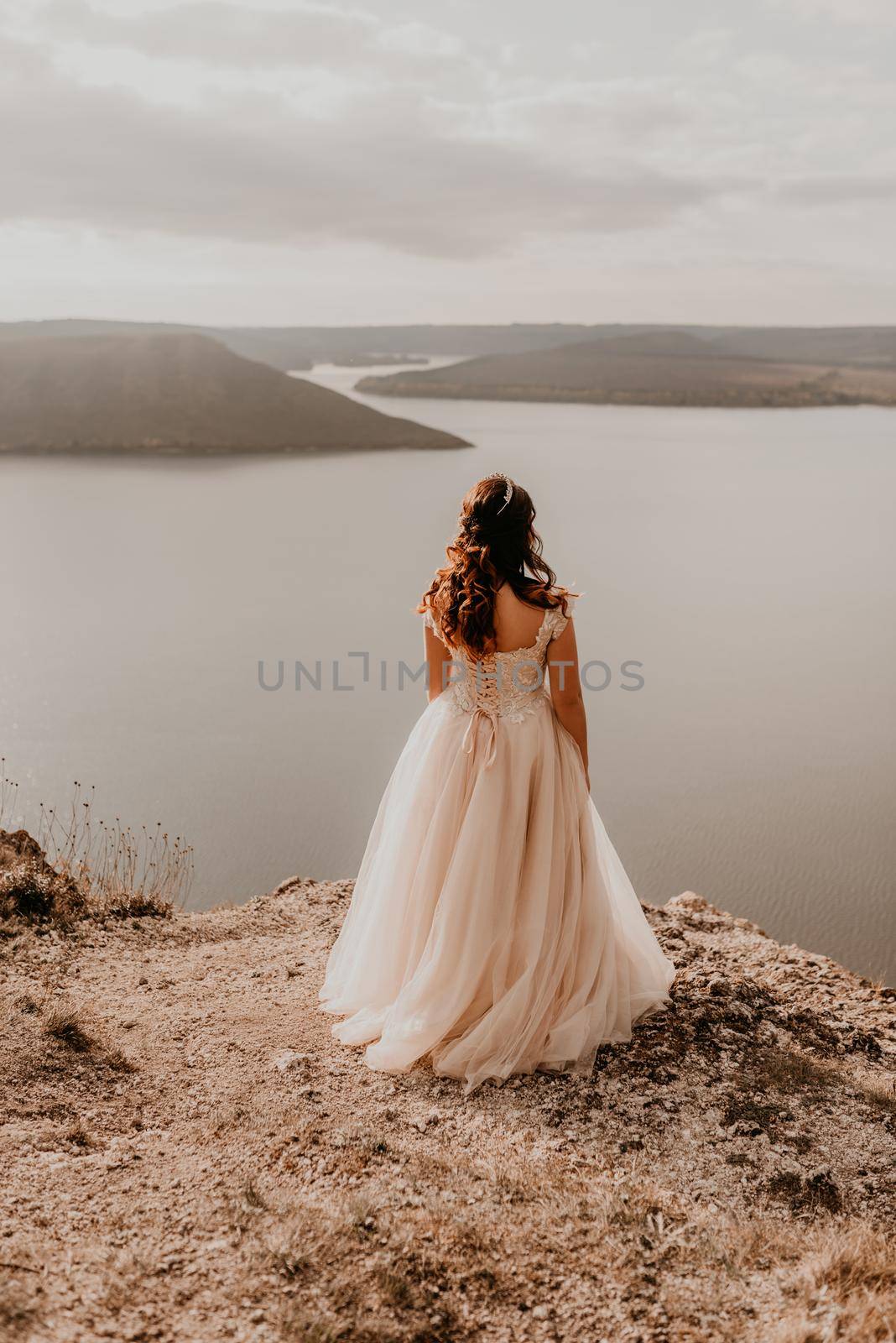 beautiful young brunette bride in a white wedding dress with a crown on her head stands on a cliff against the background of the river and islands.style fashionable women hairstyle makeup