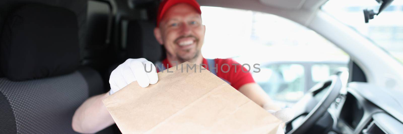 Joyful male courier giving a box while sitting in the car by kuprevich