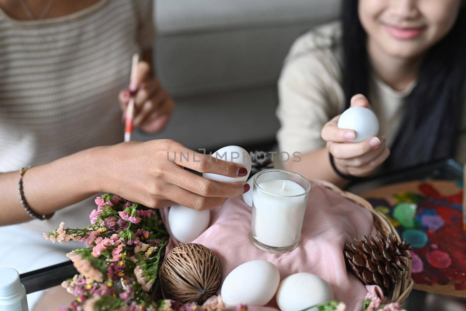 Smiling girl and mother are arranging Easter eggs into wicker basket. Happy family preparing for Easter day. by prathanchorruangsak