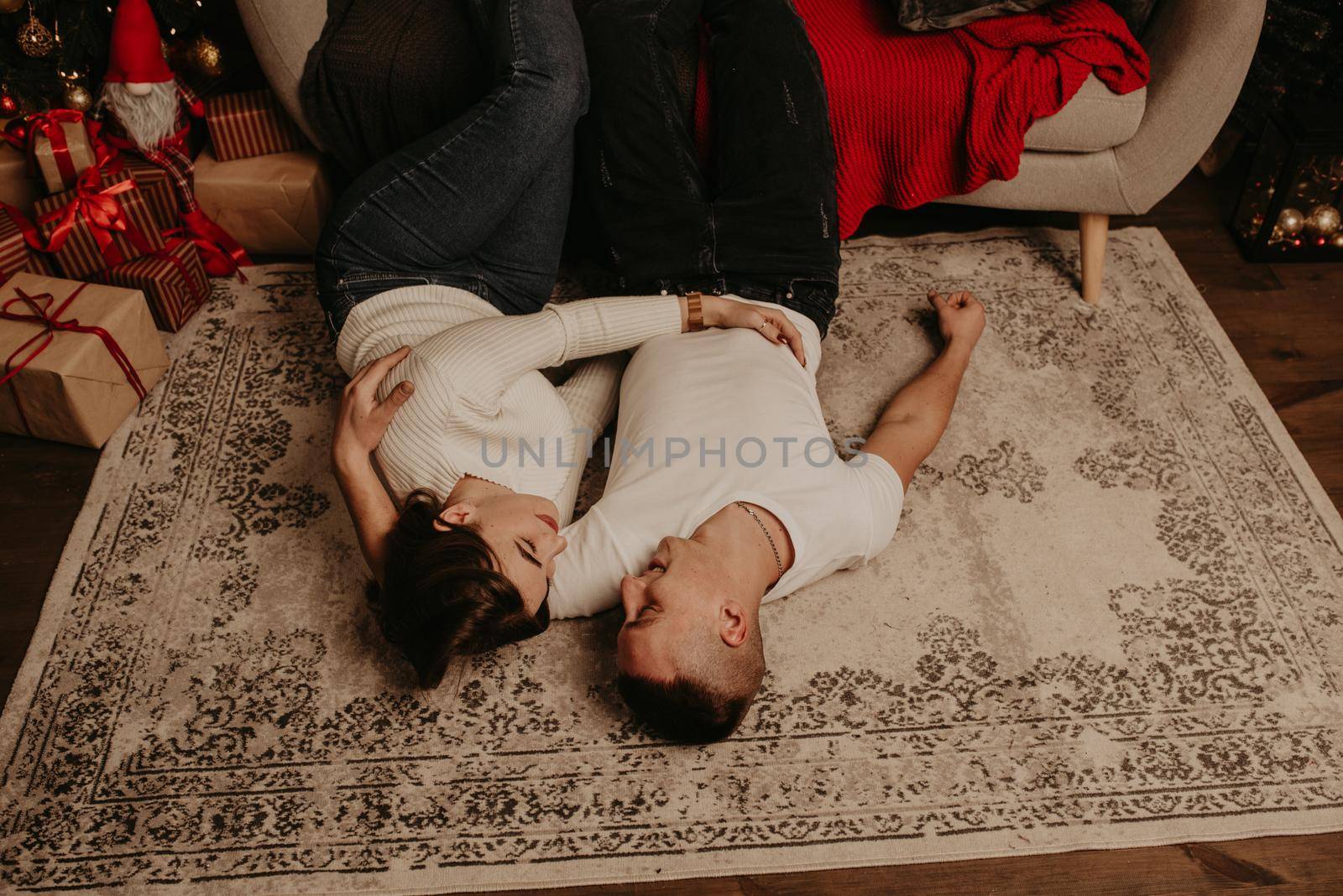 ouple lie on floor near couch with legs up kissing in the bedroom near christmas tree by AndriiDrachuk