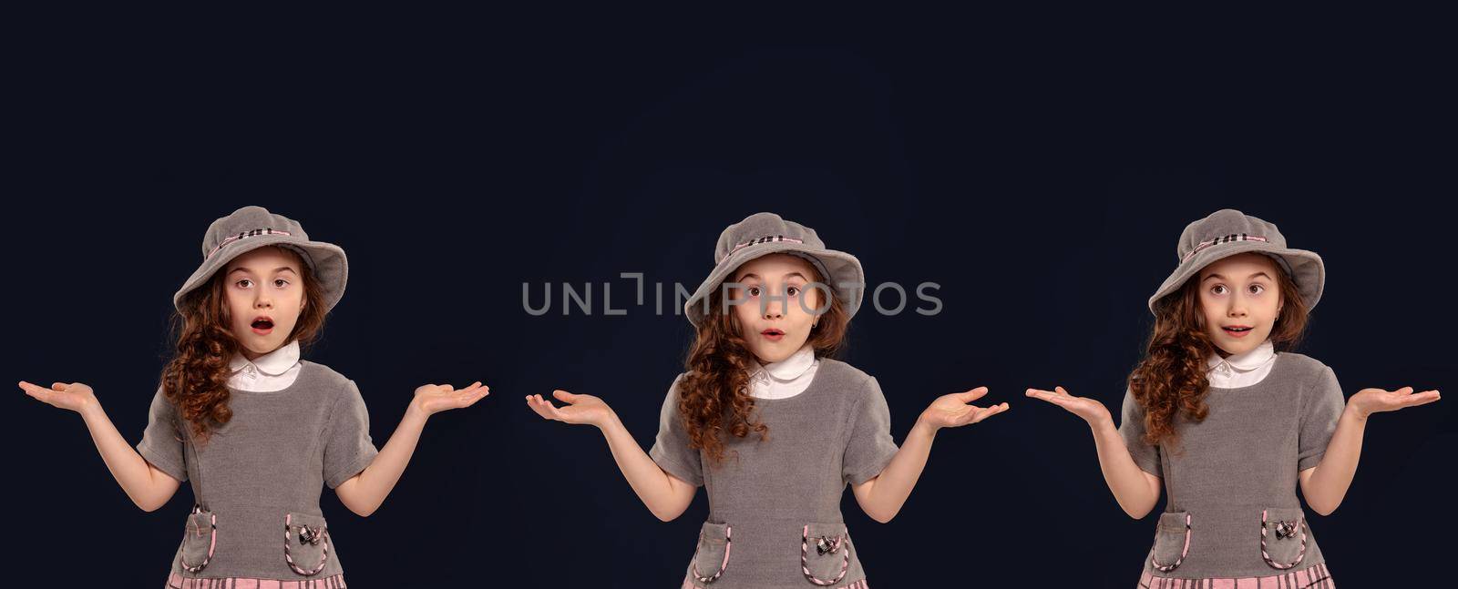 Close-up portrait of a beautiful curly little girl in a gray dress and hat looking wondered while posing on a black studio background. Set of people sincere emotions, lifestyle concept. Mockup copy space.