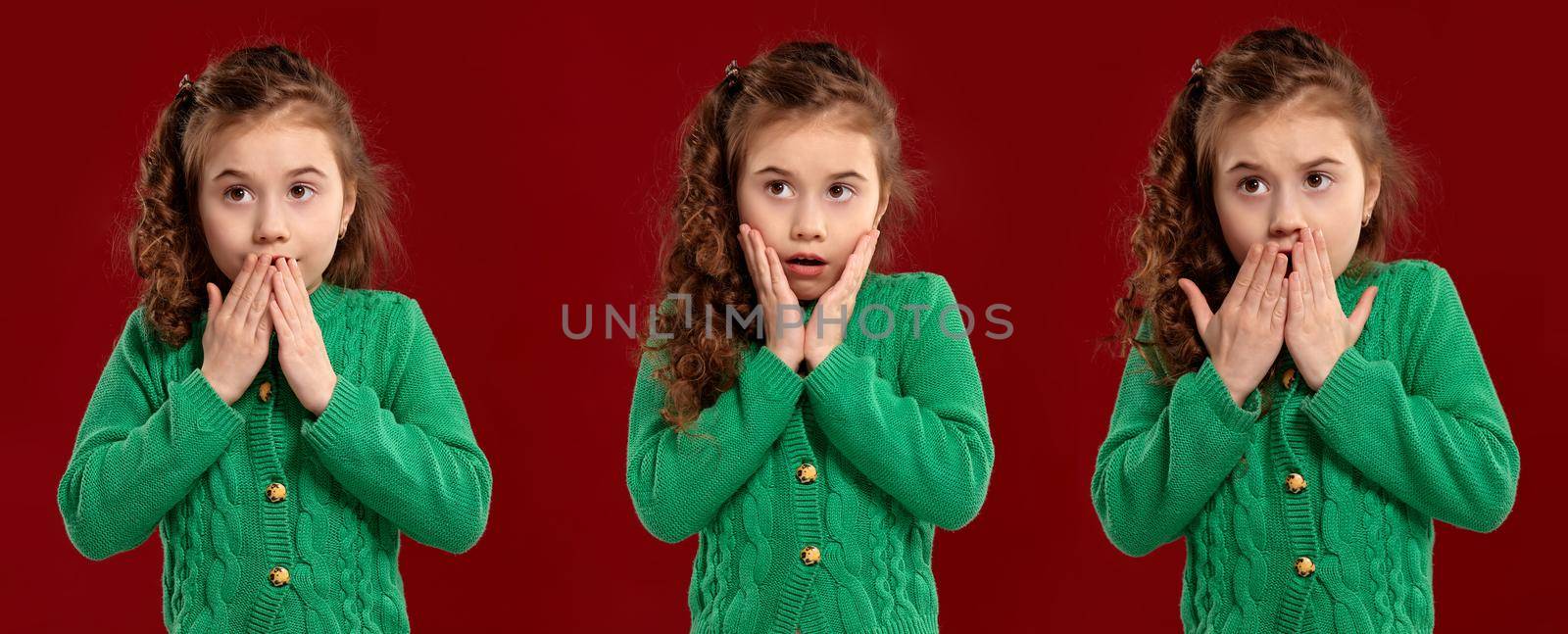 Close-up portrait of a lovely curly child in a green knitted sweater looking wondered and scared while posing on a red studio background. Set of people sincere emotions, lifestyle concept. Mockup copy space.