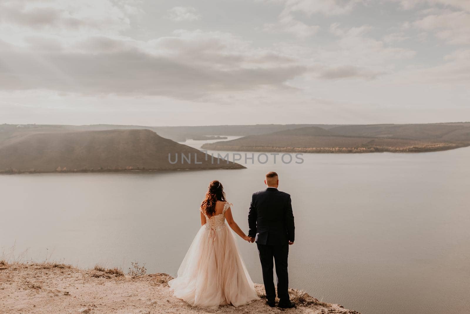 loving couple wedding newlyweds in white dress and suit walk in summer on mountain above river by AndriiDrachuk