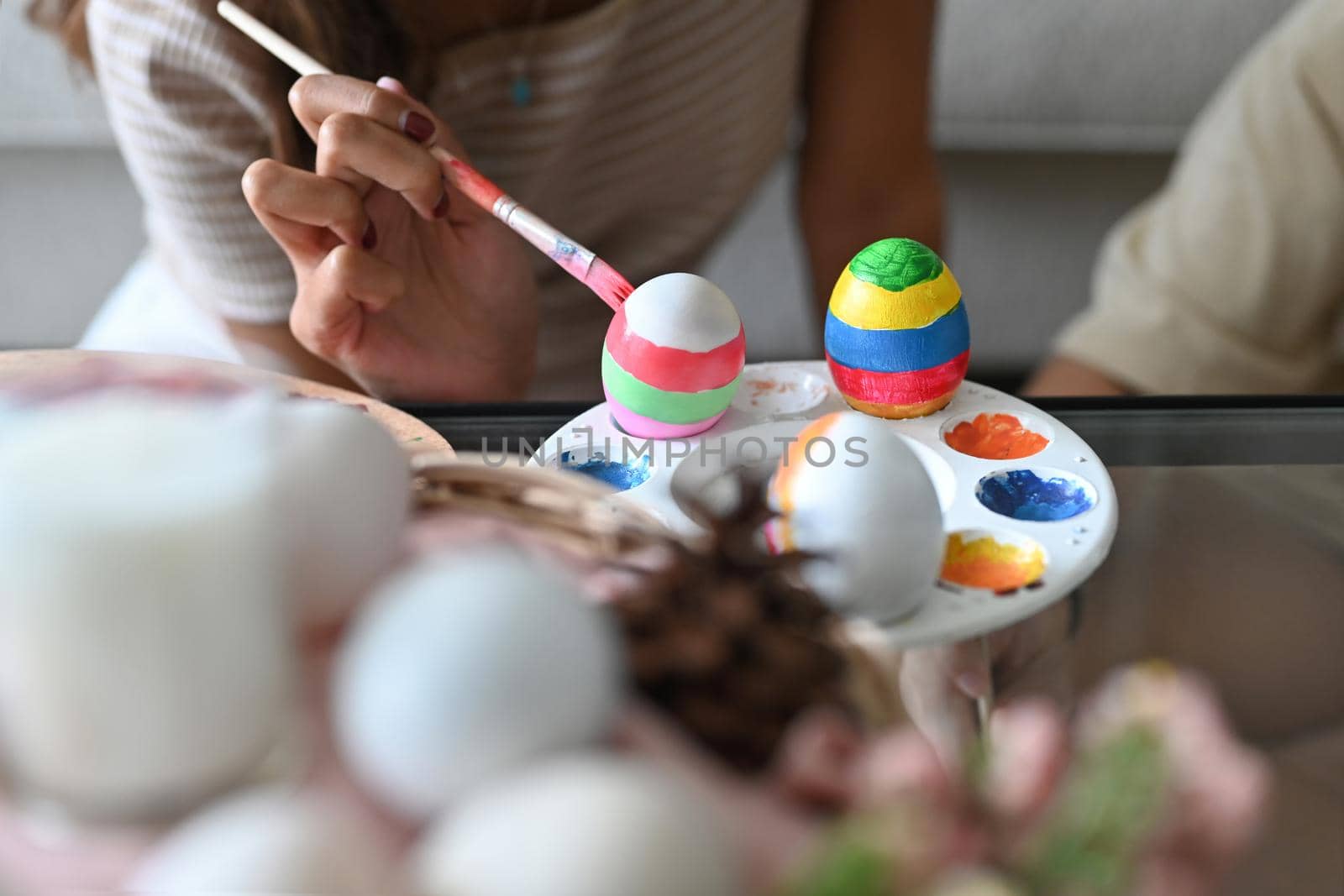Cropped shot of young woman holding paintbrush and coloring egg, preparing for Easter festival.