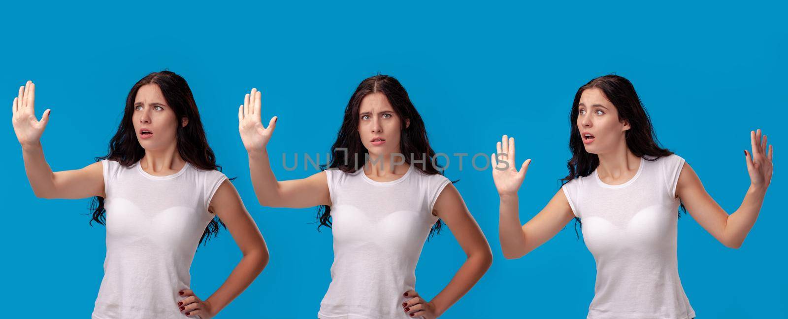 Close-up shot of a beautiful brunette woman in a white casual t-shirt posing against a blue studio background. She act like she is confused and trying to stop someone. Set of a people sincere emotions. Copy space.