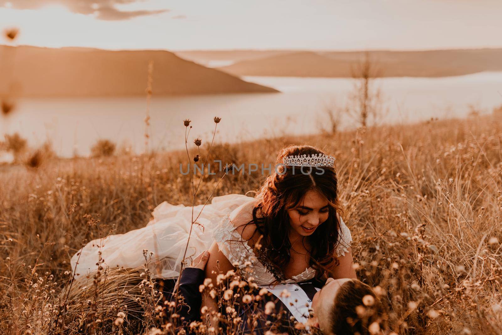couple in love wedding newlyweds in a white dress and suit are walking lying long grass field in summer. man and woman kissing. bride and groom have fallen Meadow