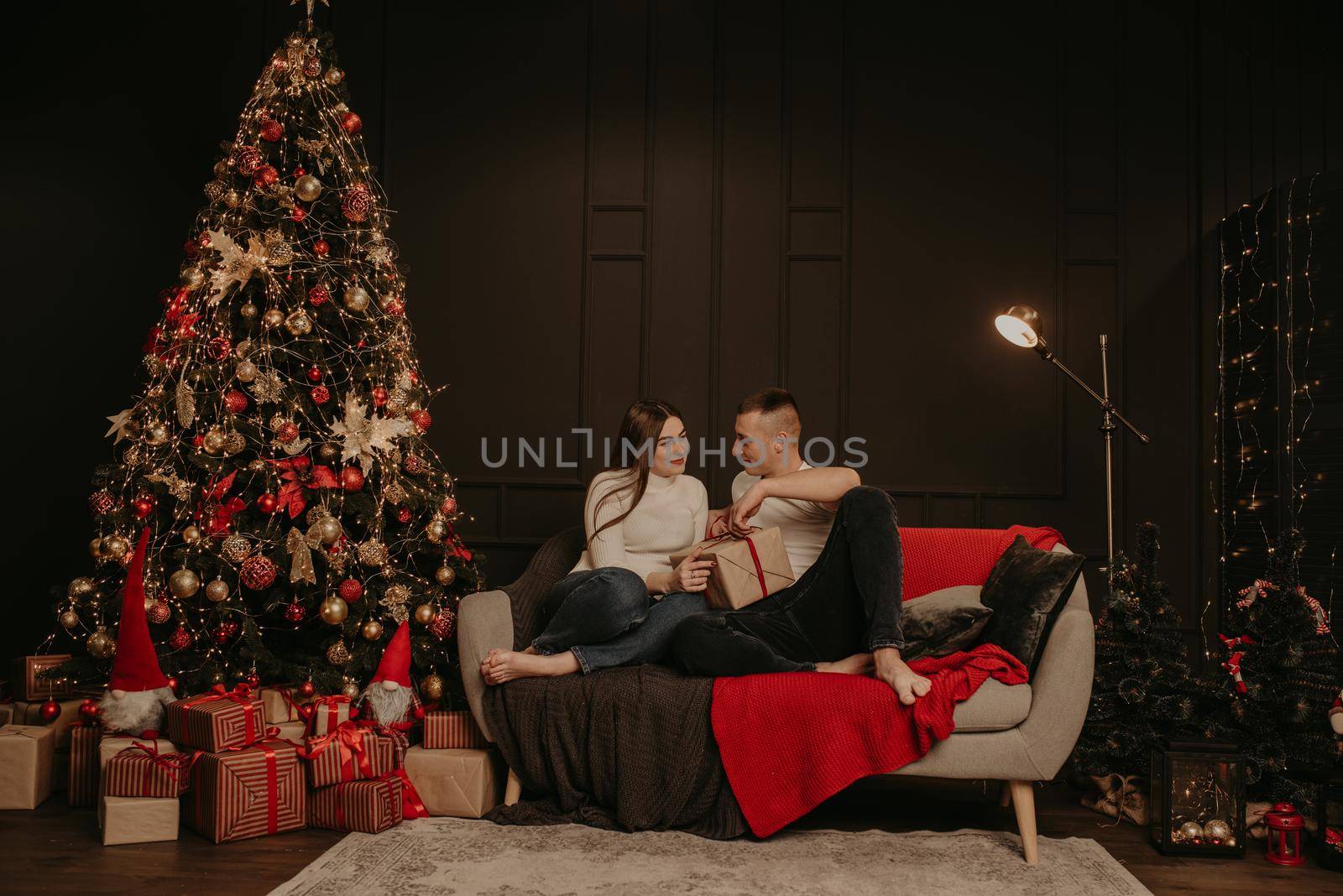 man and woman couple in love open gift boxes untie a bow near the christmas tree. decorated house for New Year. Christmas morning. apartment interior. Valentine's Day celebration