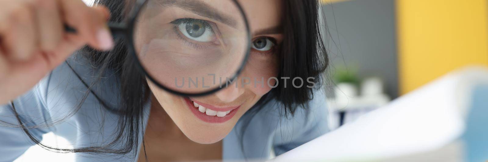 Joyful woman looks through a magnifying glass, close-up. Financial audit, detective agency, investigation, document archiving