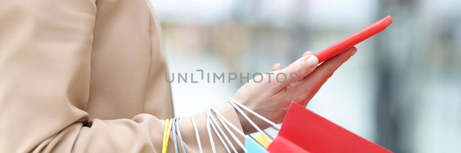 A woman holds a smartphone and packages in her hand, close-up. Online purchase, pre-order of goods, reservation. Shopaholic