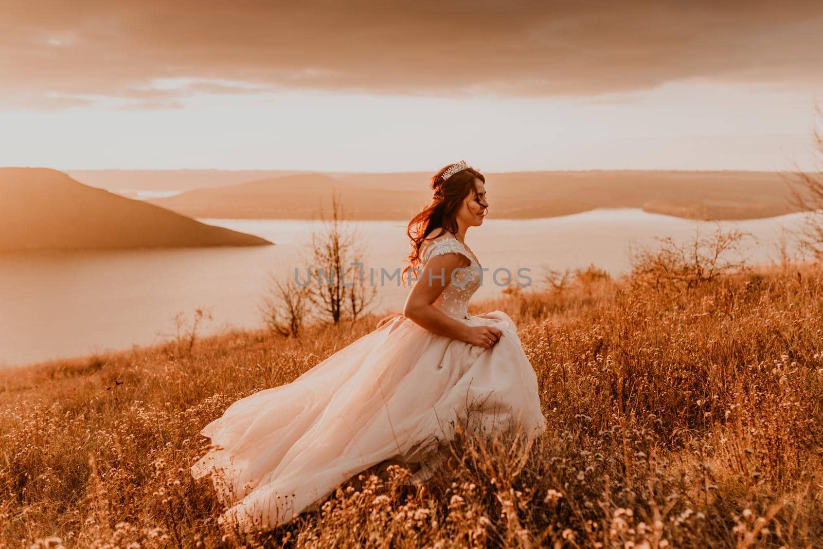 beautiful woman brunette bride in white dress and suit are walking on tall grass in field in summer