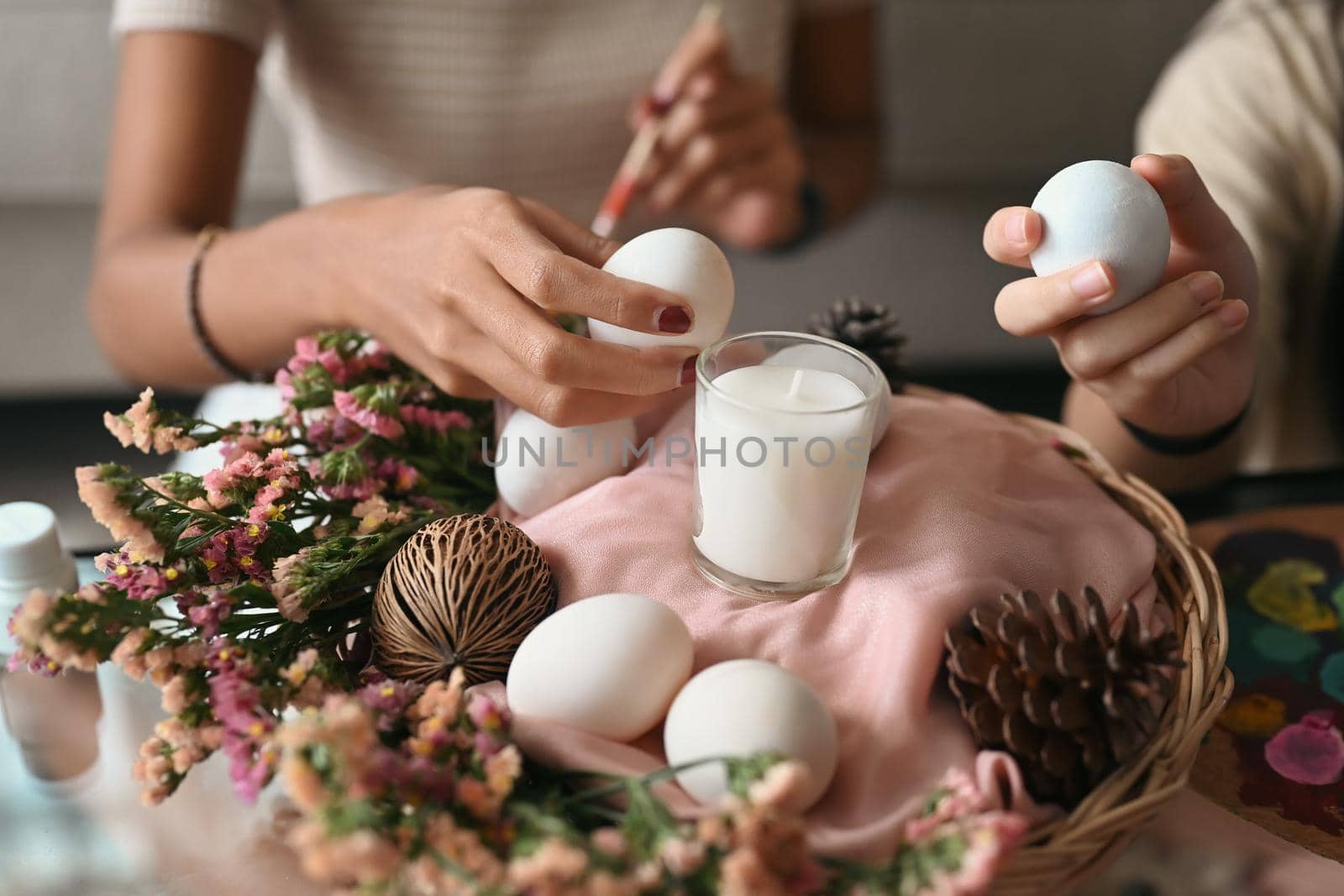 Mother and daughter are arranging Easter eggs into wicker basket and preparing for Easter celebration.