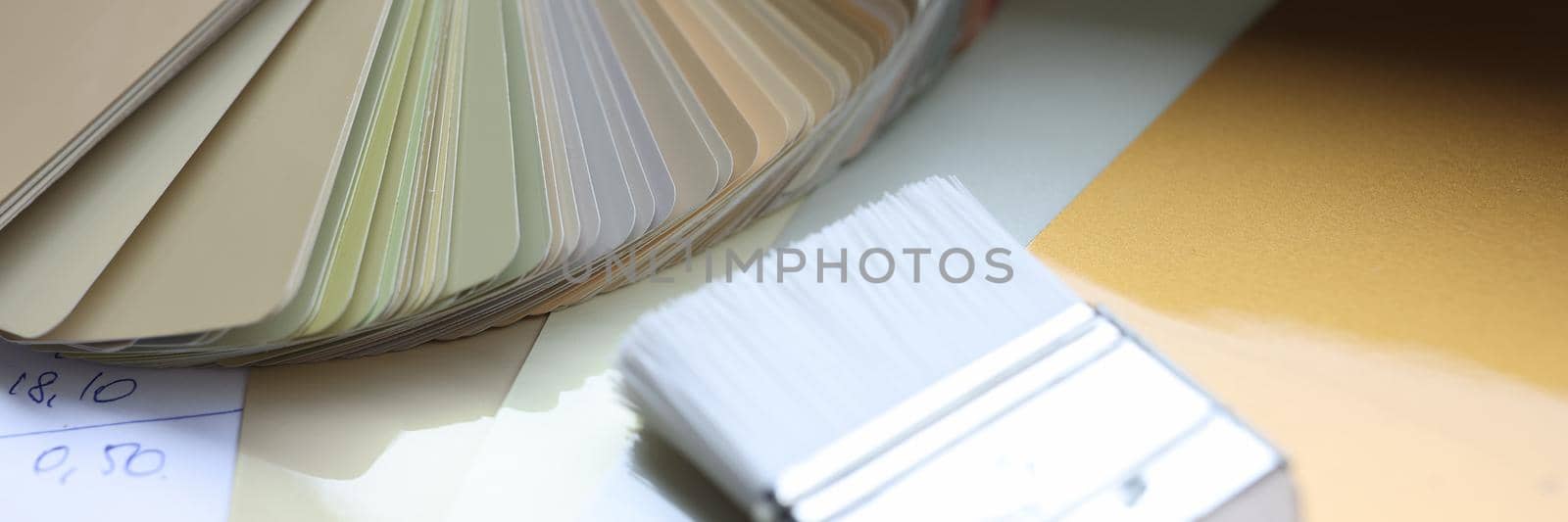 Samples of a color palette and a paint brush lie on the table, close-up. Beautiful color scheme for design, designer workspace