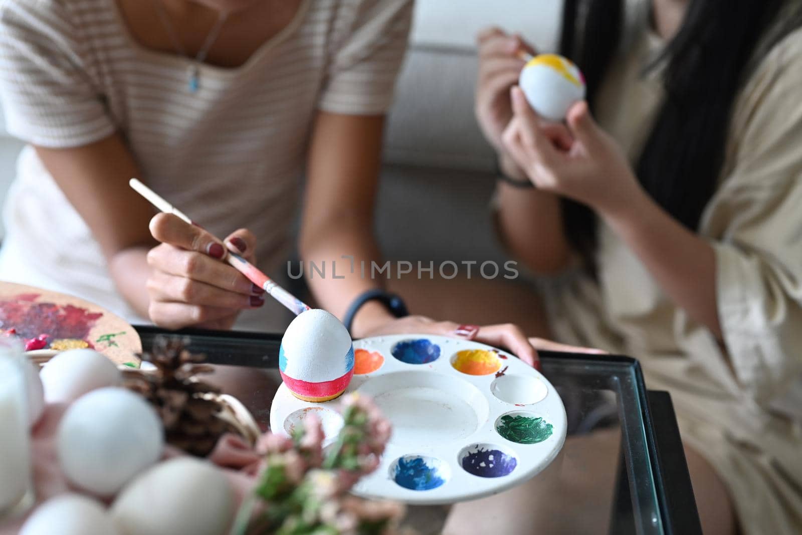 Young woman and her young sister coloring eggs, preparation for the Easter holiday. by prathanchorruangsak