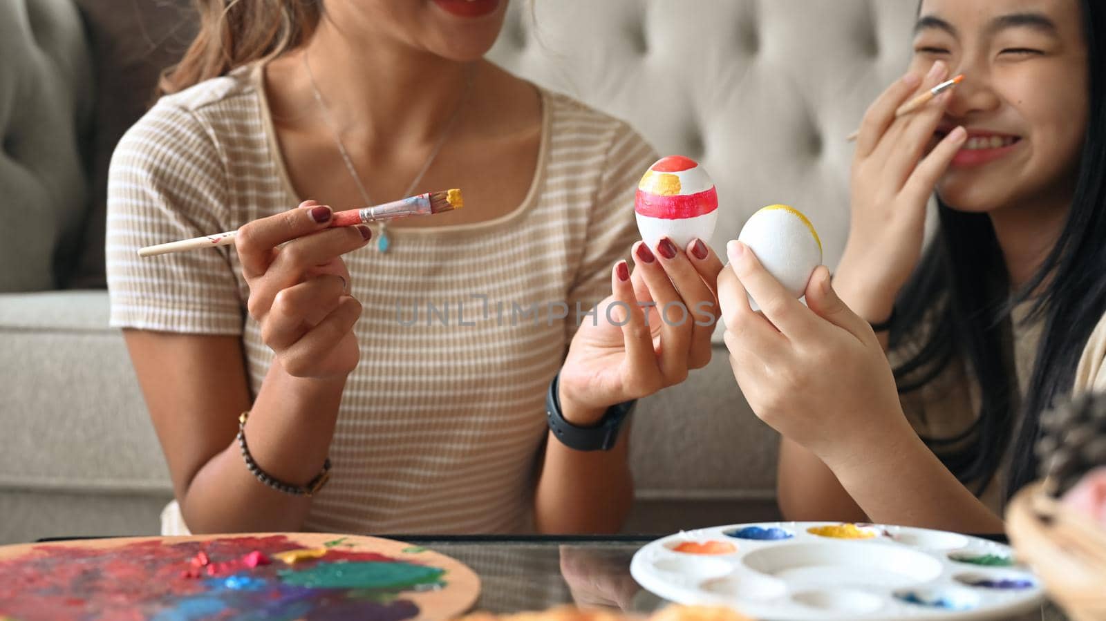 Cheerful Asian girl painting Easter eggs while enjoying decorating with mother. Easter holidays and people concept.