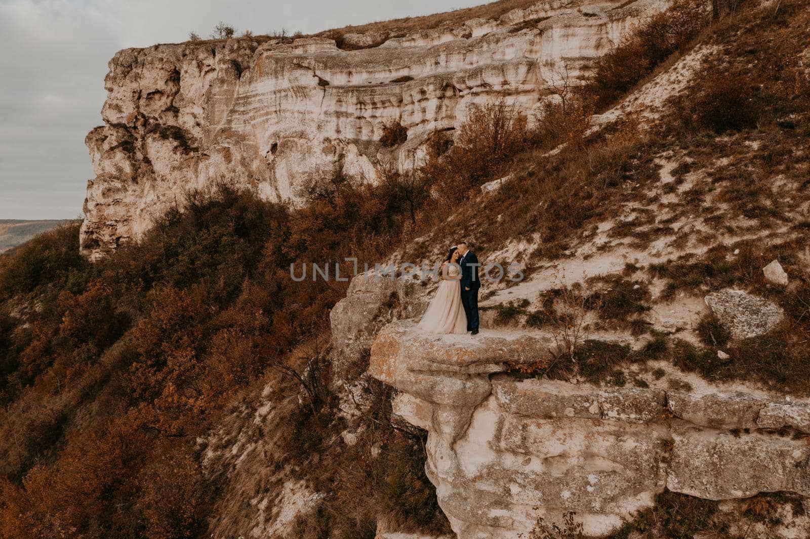 groom in suit and the bride in a dress stand on a stone cliff Aerial view from drone by AndriiDrachuk