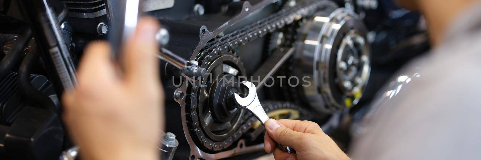 A man spins a detail on a motorcycle with a wrench, close-up. Mechanic works in a garage, maintenance and repair of a motorbike