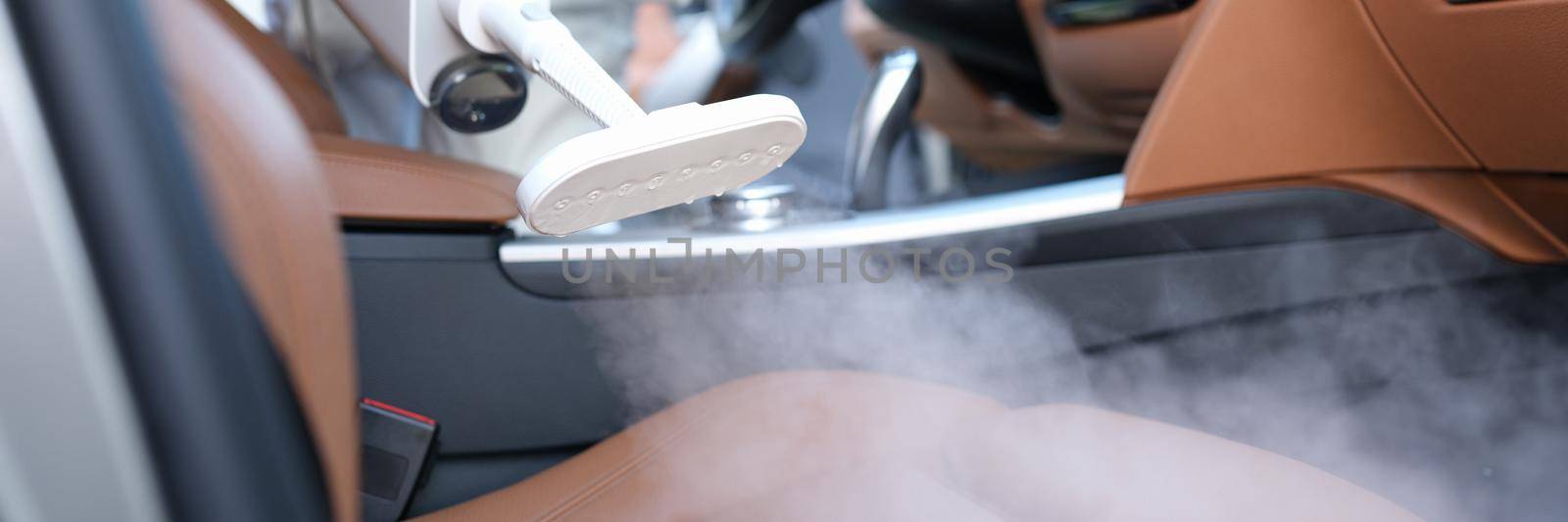 A specialist cleans a chair in a car with a washing vacuum cleaner, close-up. Steam cleaner, gentle care of the leather interior of the car