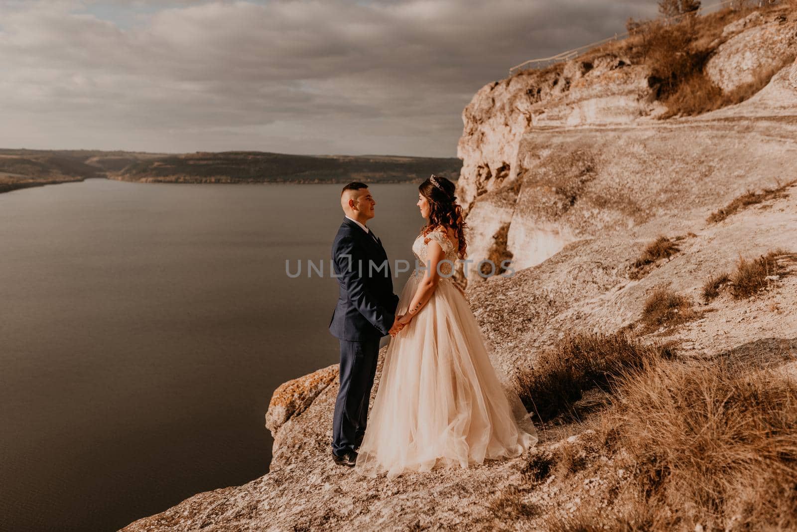 loving couple wedding newlyweds in white dress and suit walk in summer on mountain above river. sunset and sunrise. man and woman on rocks above cliff