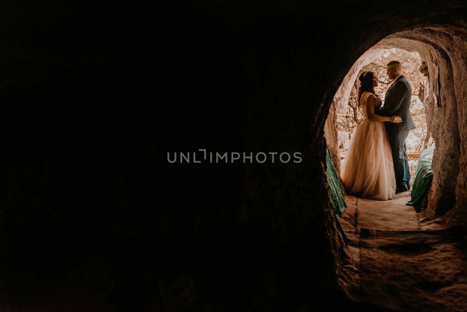 couple bride and groom in wedding dress stand in a hole in rock by AndriiDrachuk