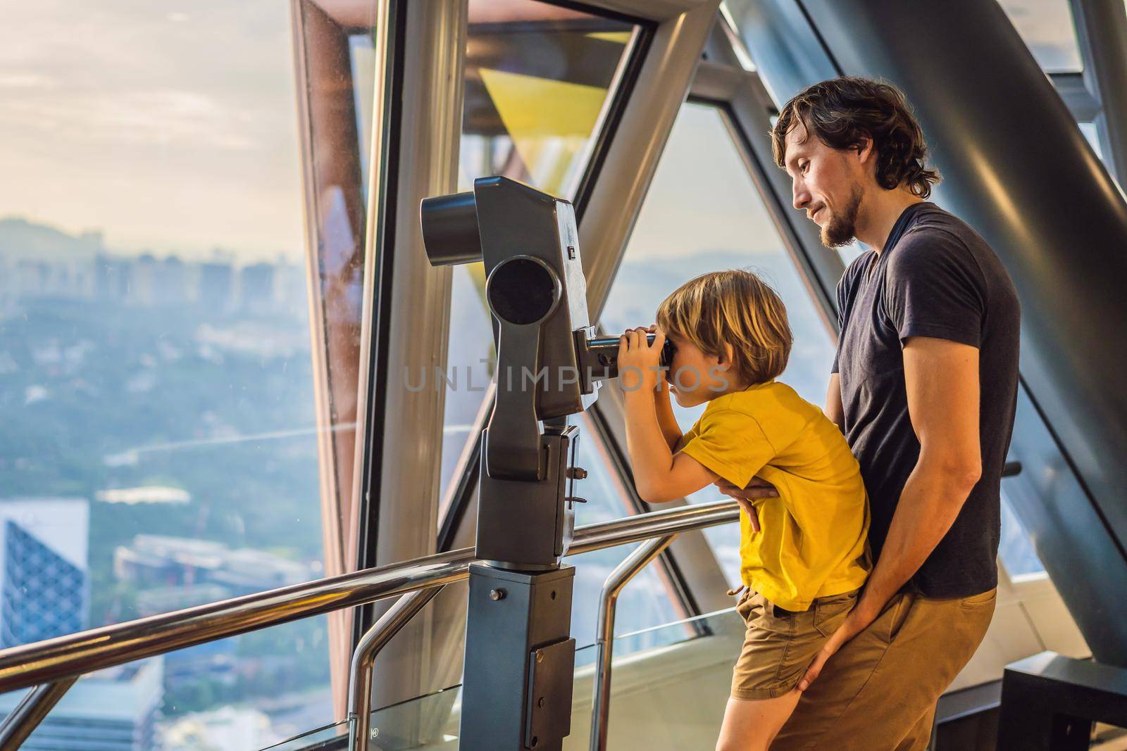 Dad and son are looking at Kuala lumpur cityscape. Us e binoculars. Panoramic view of Kuala Lumpur city skyline evening at sunset viewing skyscrapers building in Malaysia. Traveling with kids concept.