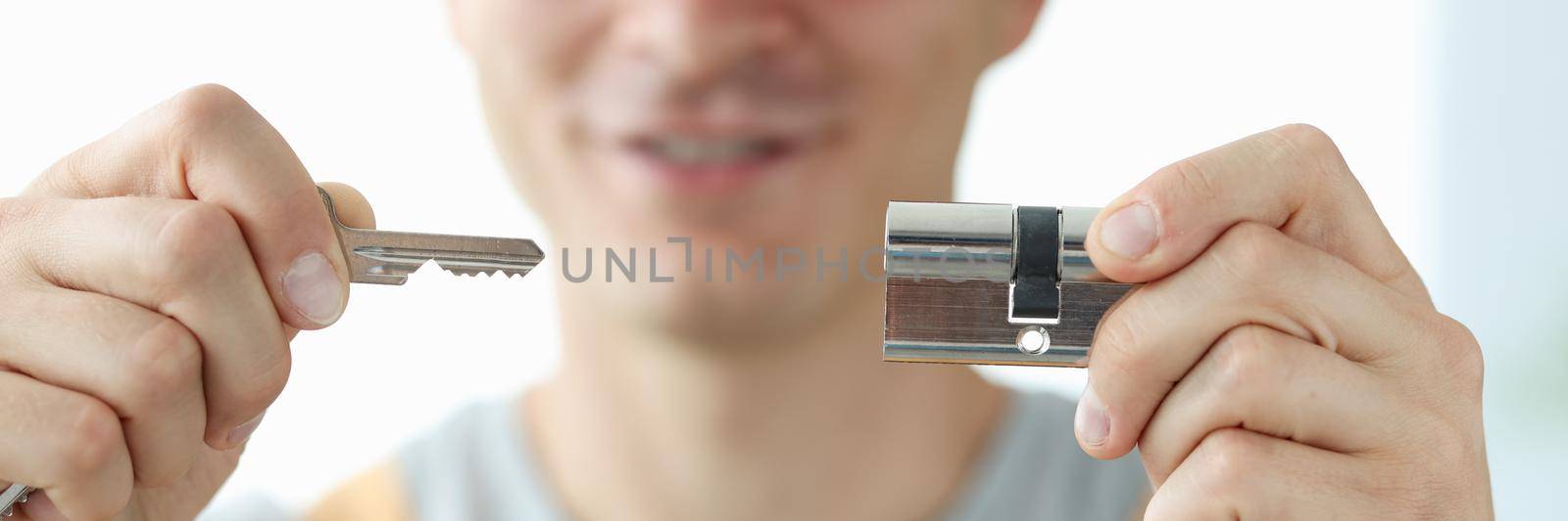 Joyful male locksmith shows a key and a lock, close-up. Apartment castle renovation, protection