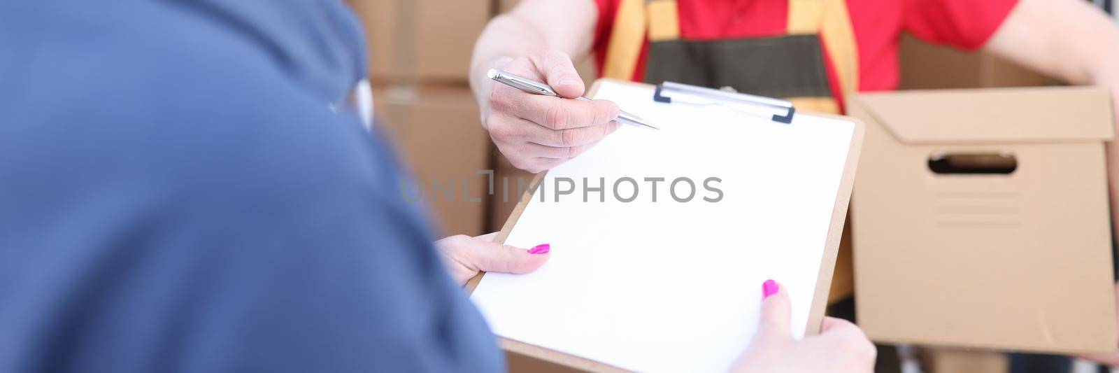 The courier holds the parcel, the woman signs the document, address delivery. Cargo transportation, truck with boxes