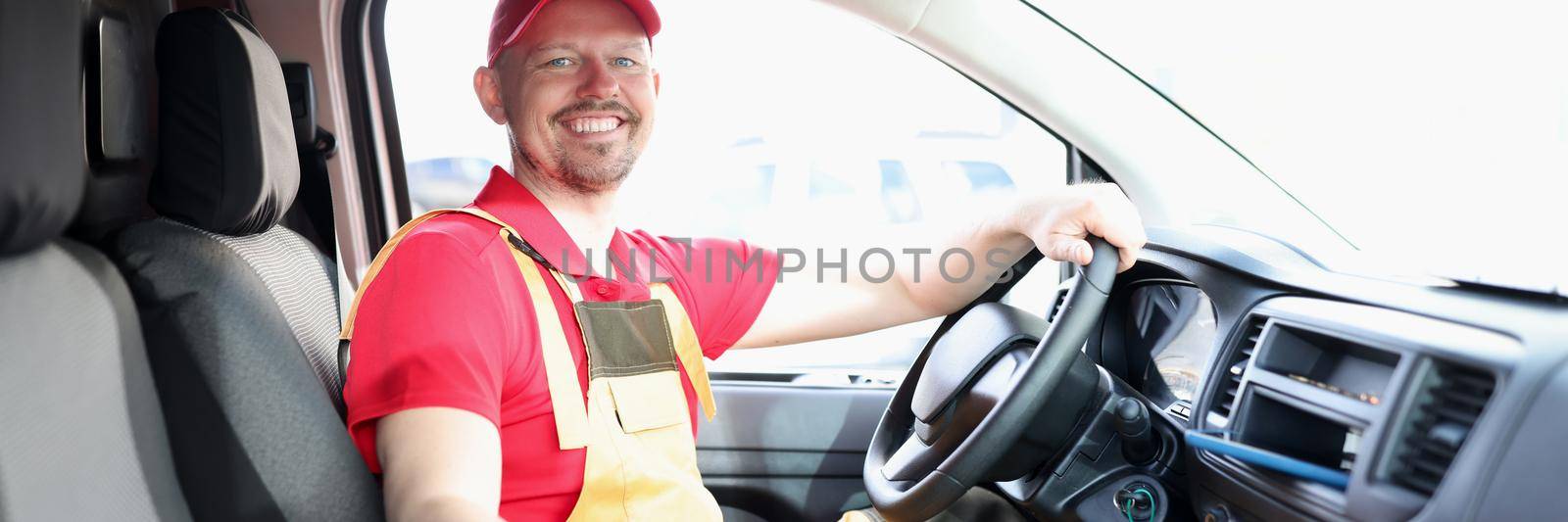 Unshaven male courier sitting in the car smiling, close-up. Deliveryman driver signs documents, shipment